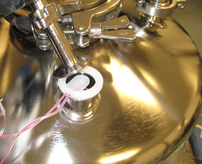 Close-up of thermocouple inserted through sanitary fitting into stainless steel vessel for steam sterilization validation.